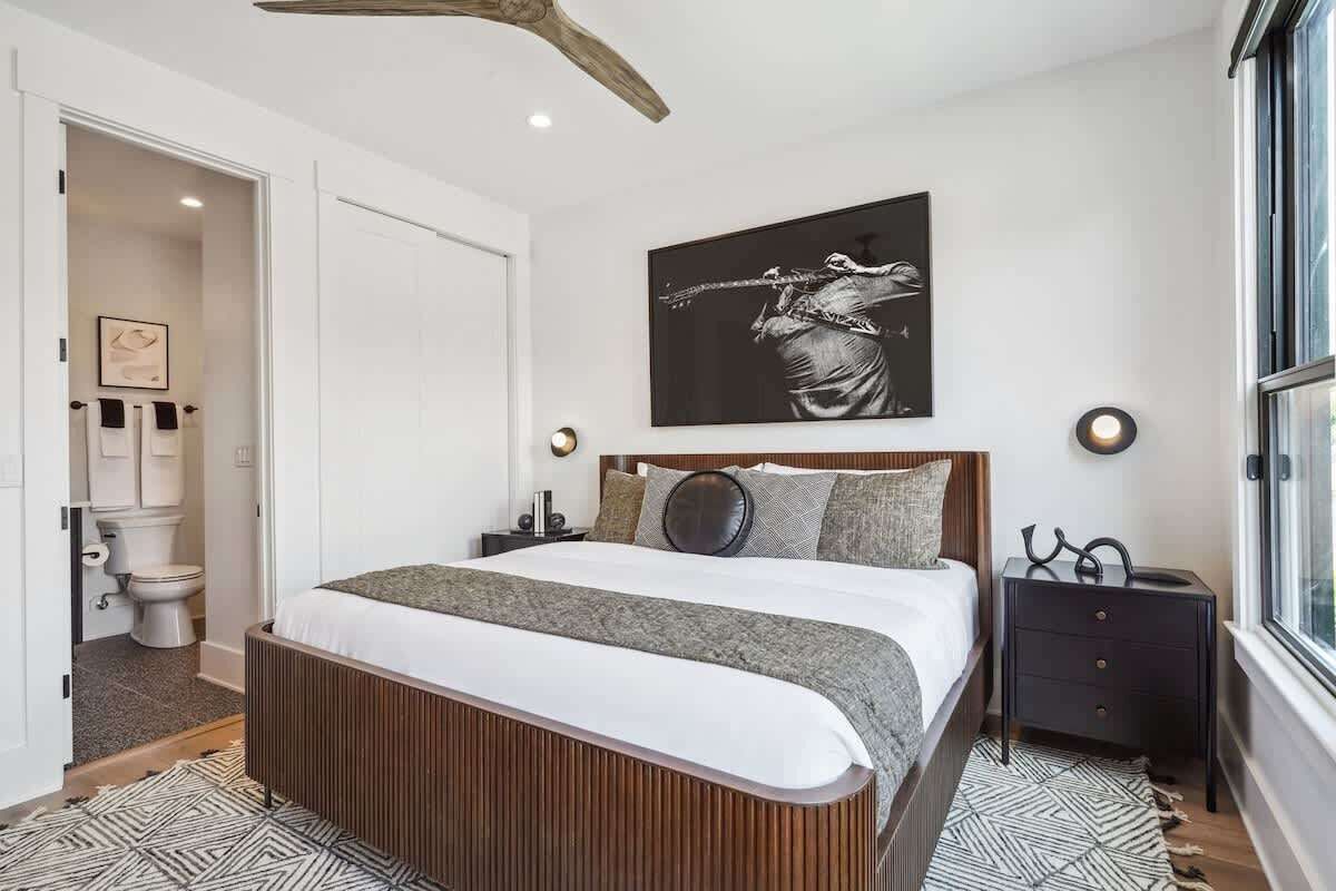 Ein modernes Schlafzimmer mit einem großen Bett, einem hölzernen Kopfteil, einem schwarz-weißen abstrakten Gemälde und einem Nachttisch mit Lampe.