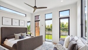 Een moderne slaapkamer met een groot bed, een bank en een balkon met uitzicht op groen.
