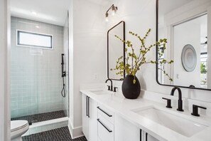 Un baño moderno con ducha, inodoro y tocador con espejo y florero.