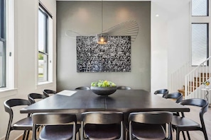 A modern dining area with a long table, black chairs, and a unique wall art piece above the table.
