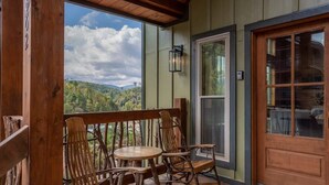 A wooden deck with a view of a mountainous landscape, a wooden rocking chair, a table, and a door with glass panels. - Mountain Views/Near DwTn Gat/New (Gatlinburg)
