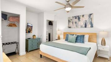 A bedroom with a bed, bedside lamps, a ceiling fan, a wardrobe, and a painting on the wall.