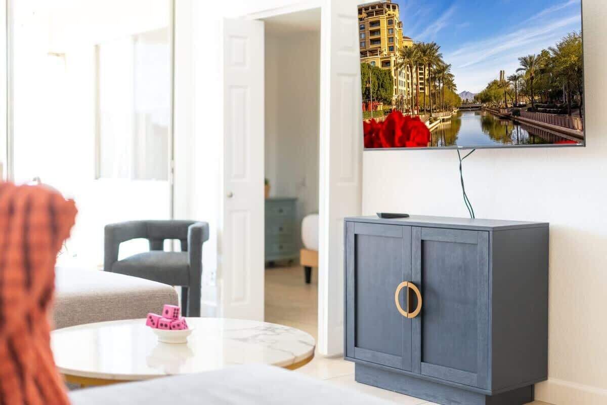 Un salon moderne avec un canapé, une petite table ronde et un meuble sur lequel est fixée une télévision diffusant une vue sur la ville.
