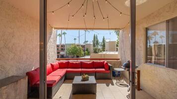 Un espace extérieur ensoleillé, aménagé avec un canapé rouge, une petite table et un barbecue.
