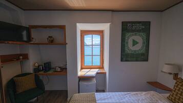 Un dormitorio con cama, escritorio con computadora, una silla, ventana con vista y un cartel en la pared.