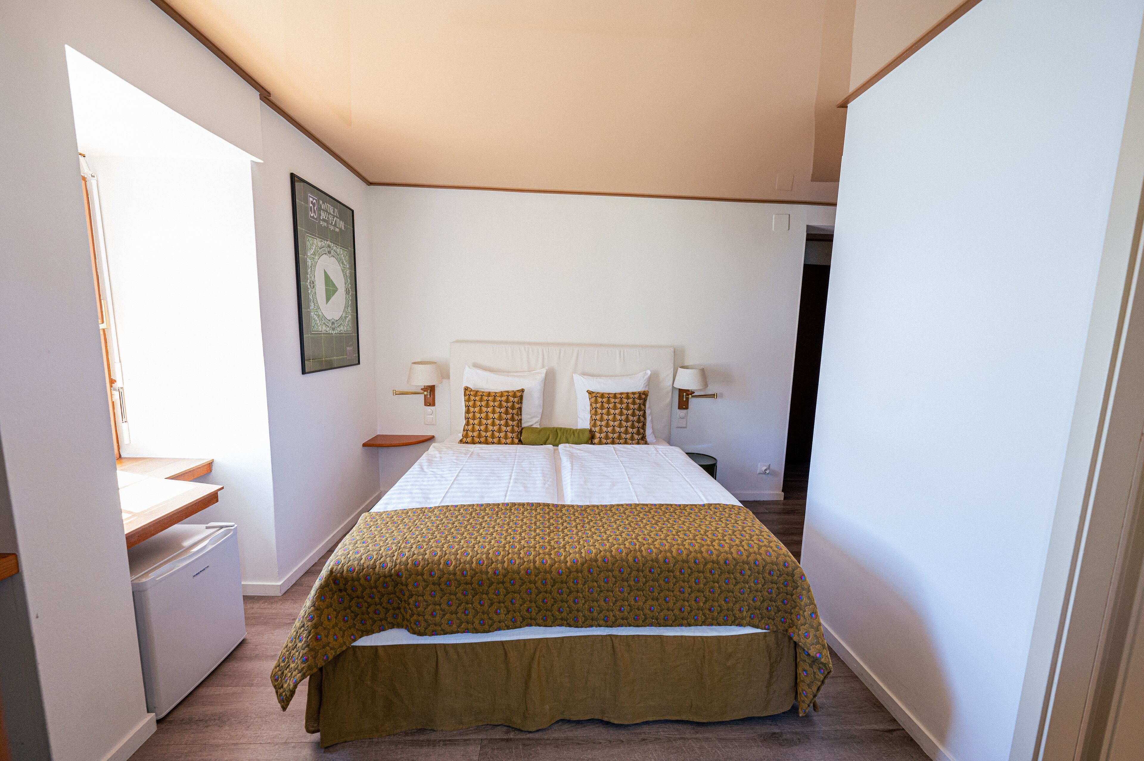 A bedroom with a bed, bedside lamps, a small table, and a window.