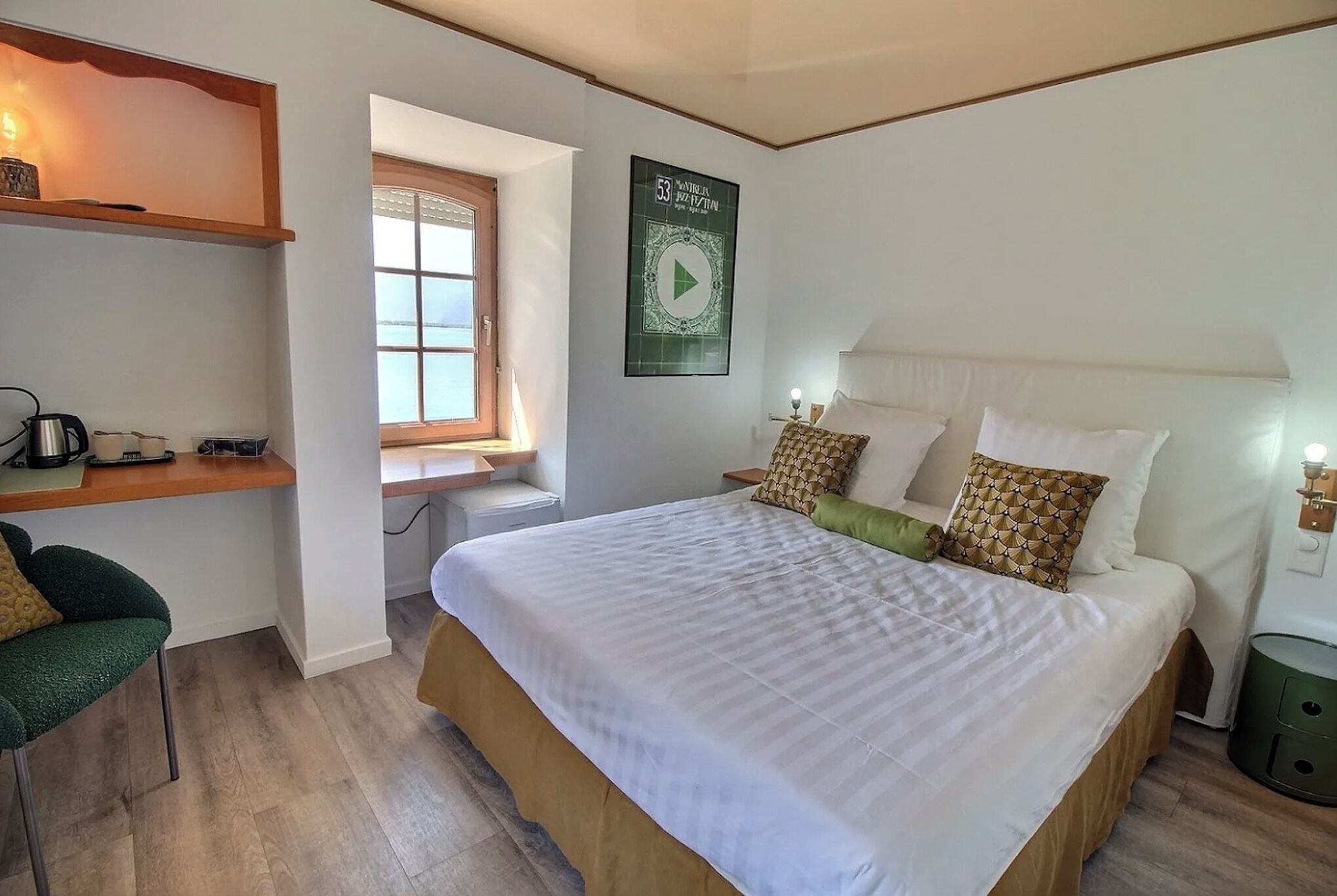 Une chambre avec un grand lit, un bureau avec une chaise, une fenêtre et une affiche accrochée au mur.