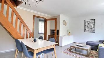 Un espacio de estar moderno con una escalera de madera, una zona de comedor con mesa y sillas, un sofá y una mesa auxiliar.