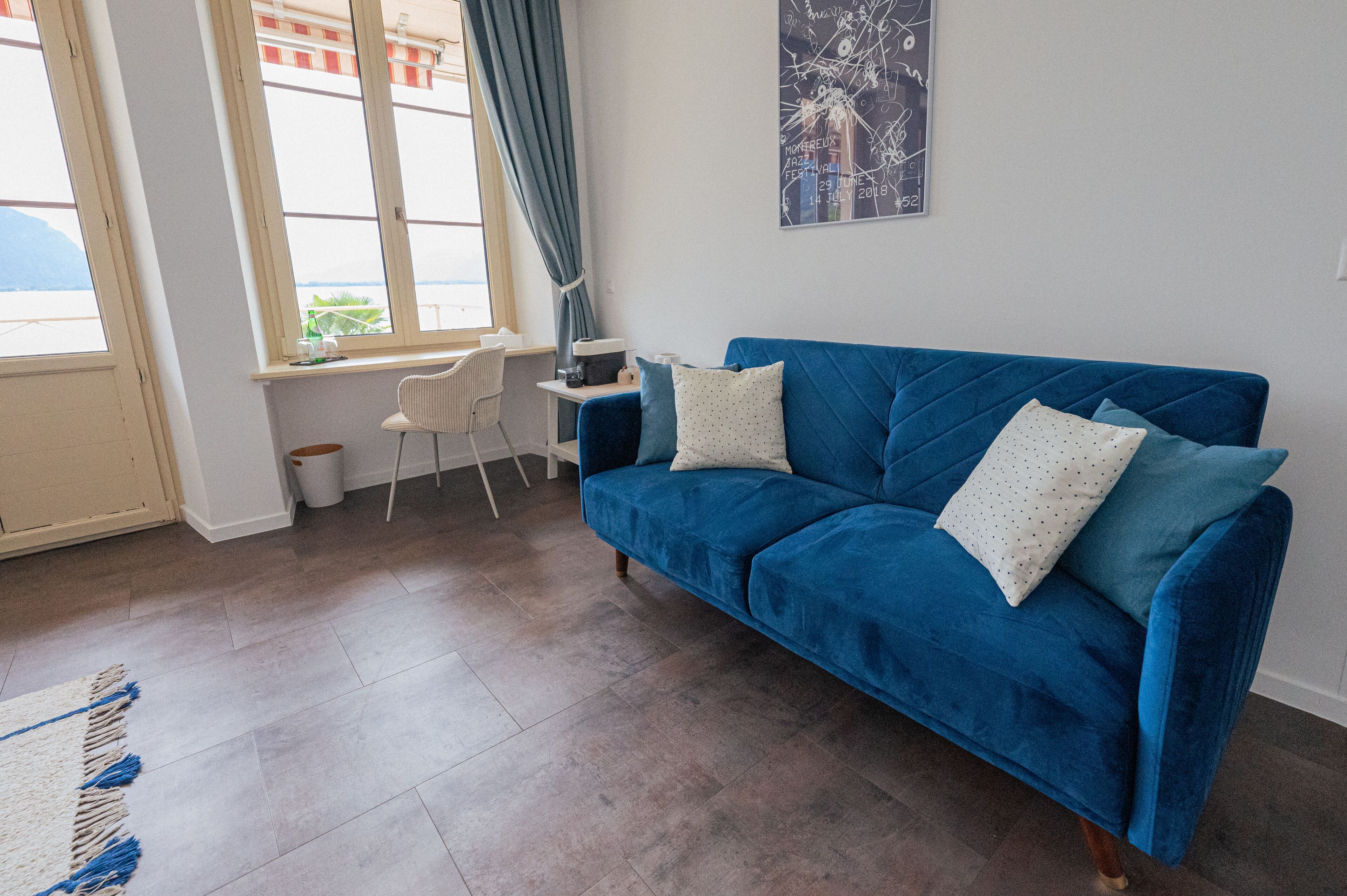 A room with a blue sofa, a small table, a chair, and a window with a view.