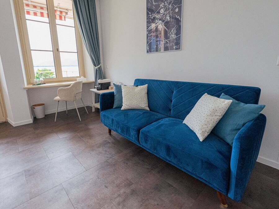 Una habitación con un sofá azul, una mesita, una silla y una ventana con vistas.