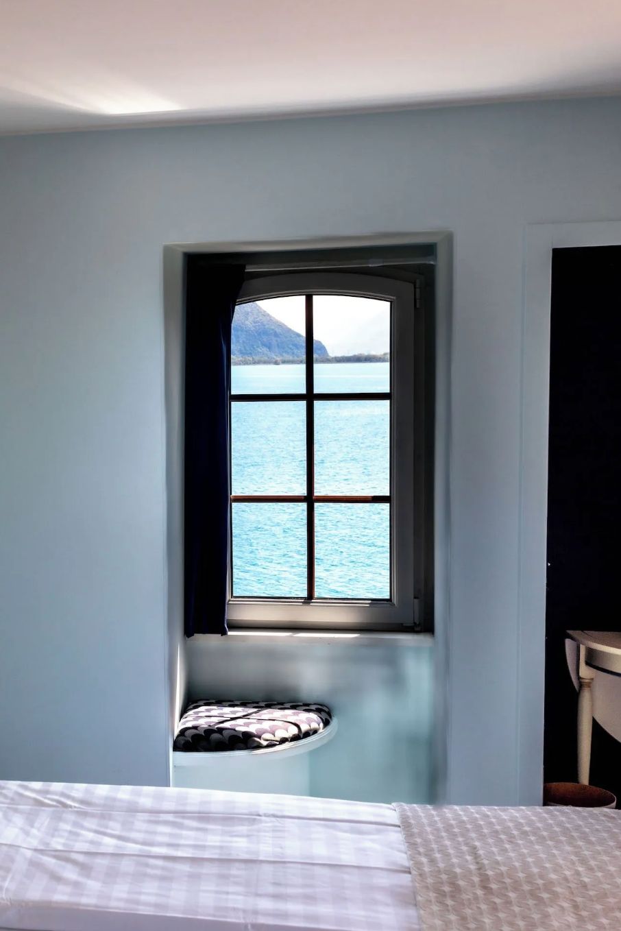 A bedroom with a window offering a view of a body of water and a mountain.