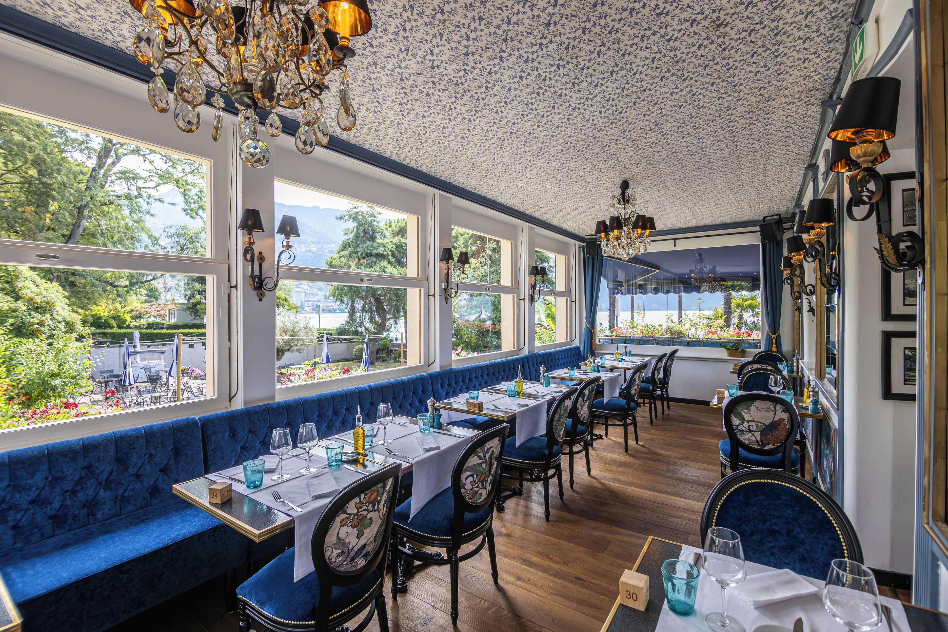 Un restaurante con asientos tapizados en azul, mesas blancas y candelabros.