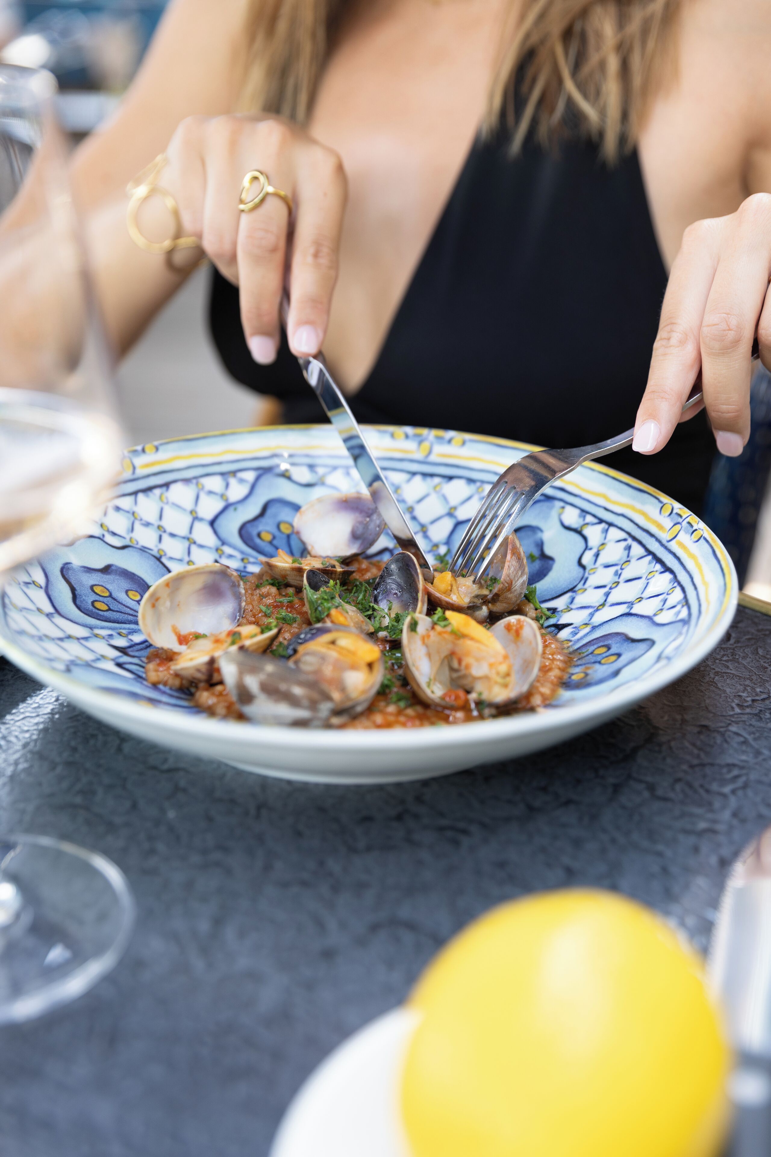 Un piatto di vongole con forchetta e cucchiaio, un bicchiere d'acqua e un limone su un tavolo.