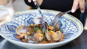 Un piatto di vongole con forchetta e cucchiaio, un bicchiere d'acqua e un limone su un tavolo.