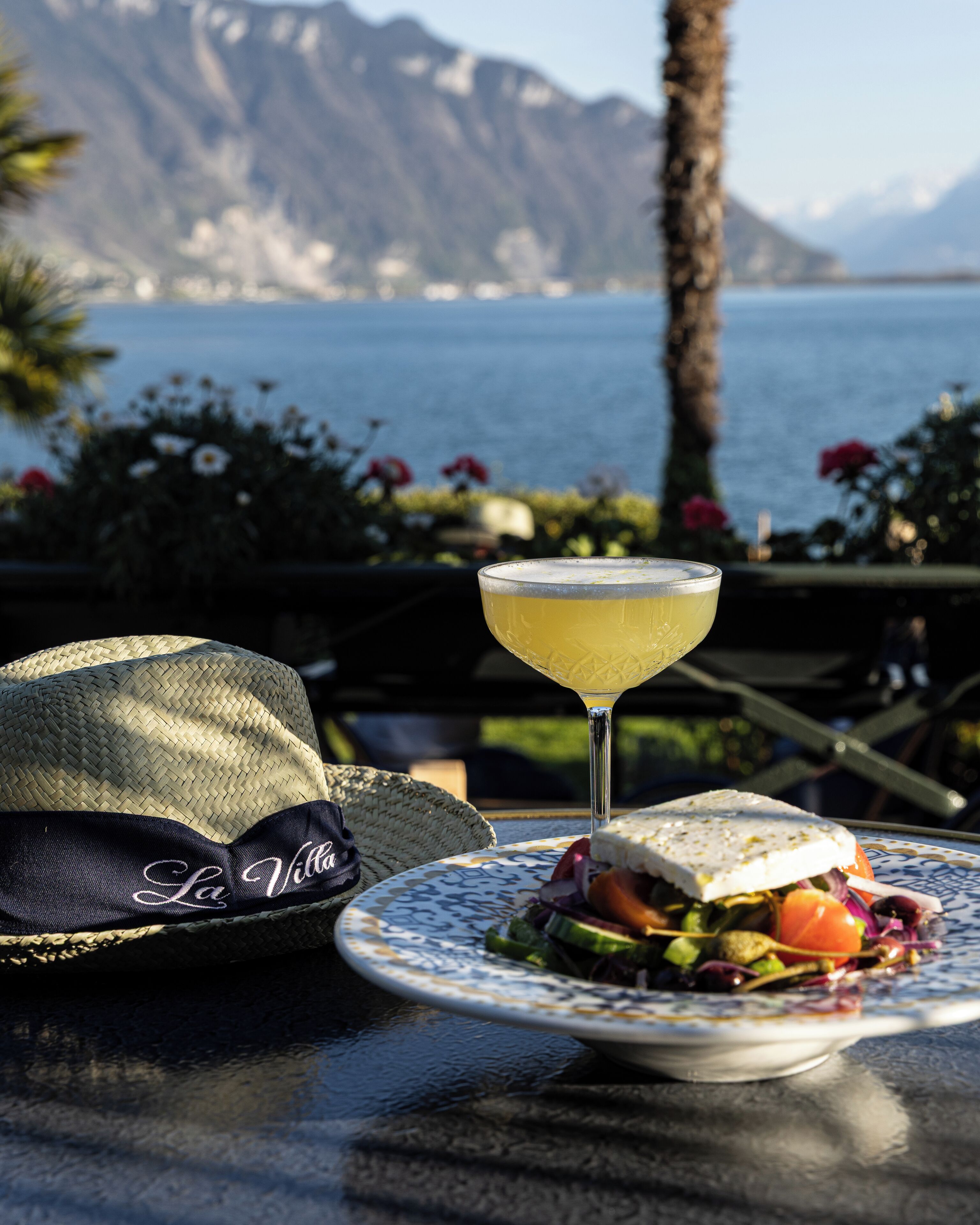 Ein Tisch mit Hut, einem Getränk und einem Teller mit Sandwich und Salat.