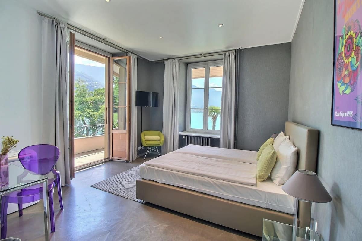 Ein modernes Schlafzimmer mit einem großen Bett, einem Fernseher, einem Sessel und Blick ins Freie.