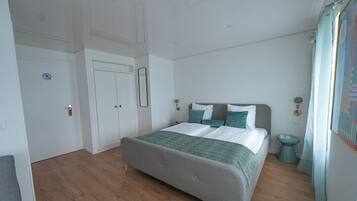 A bedroom with a bed, a door, a mirror, and a nightstand.