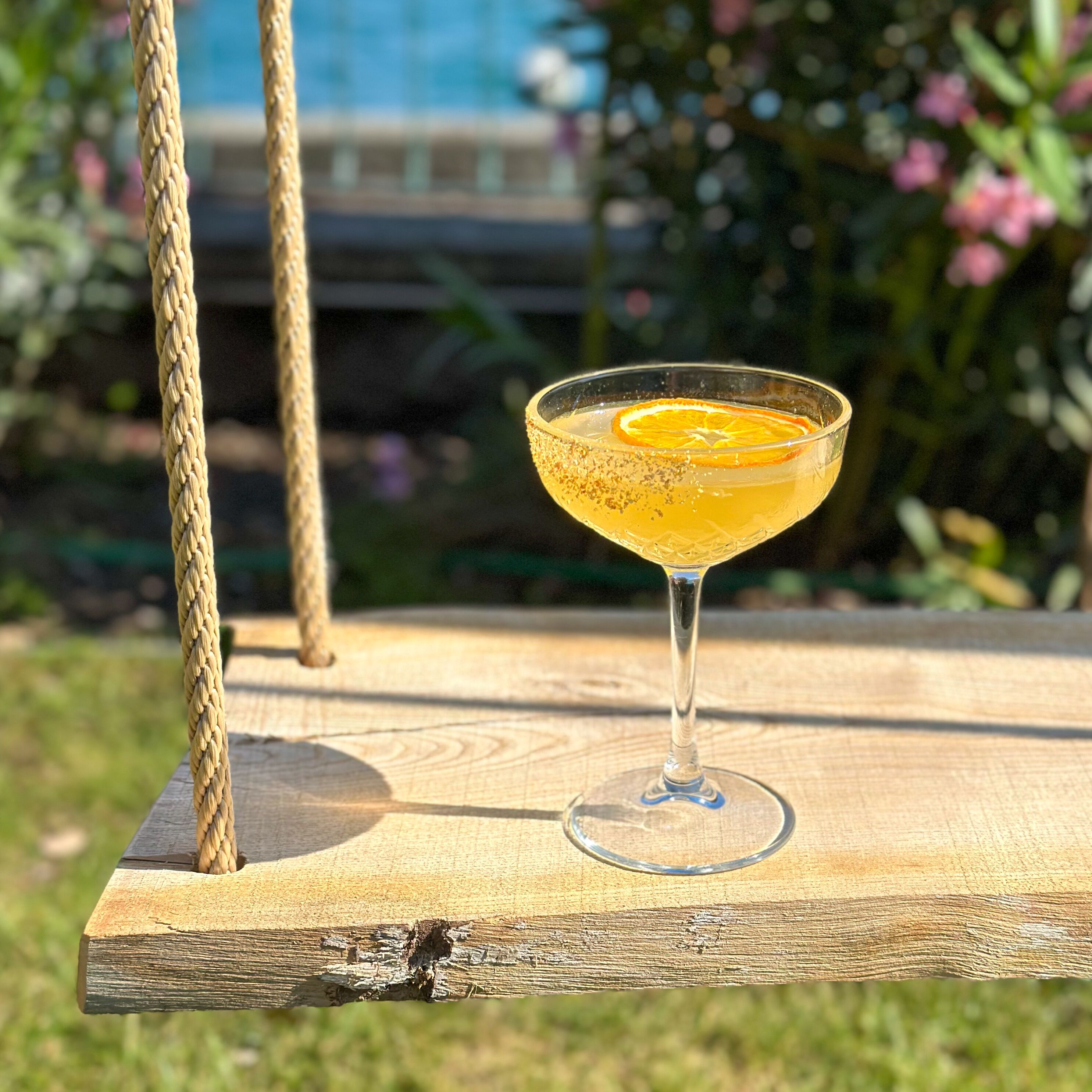 Un vaso de cóctel con una rodaja de naranja en una silla mecedora de madera al aire libre.
