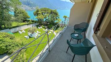 Un balcon avec vue sur un lac et des montagnes, des chaises vertes et une petite table.