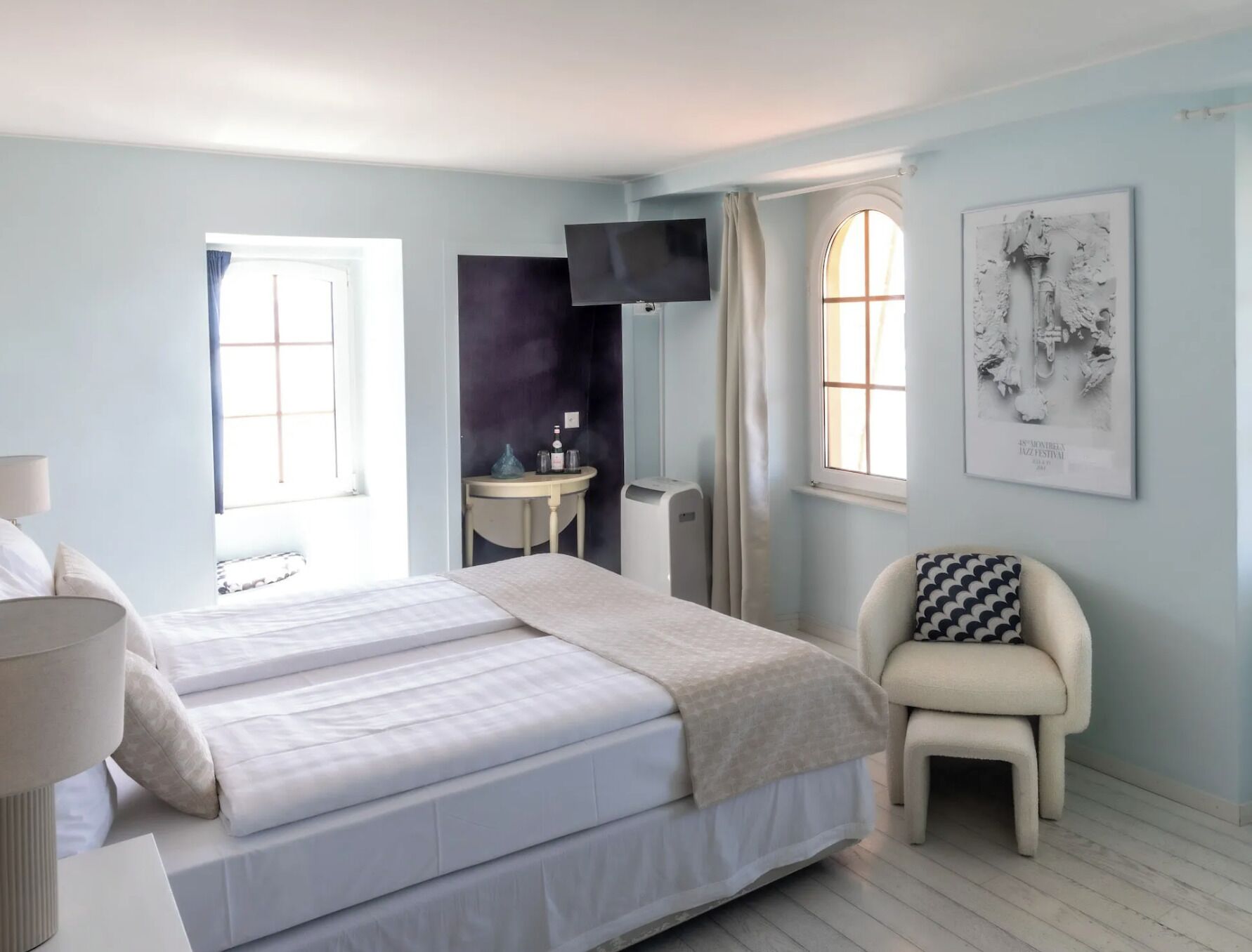 A bedroom with a bed, a bedside table, a chair, a TV, and a window.