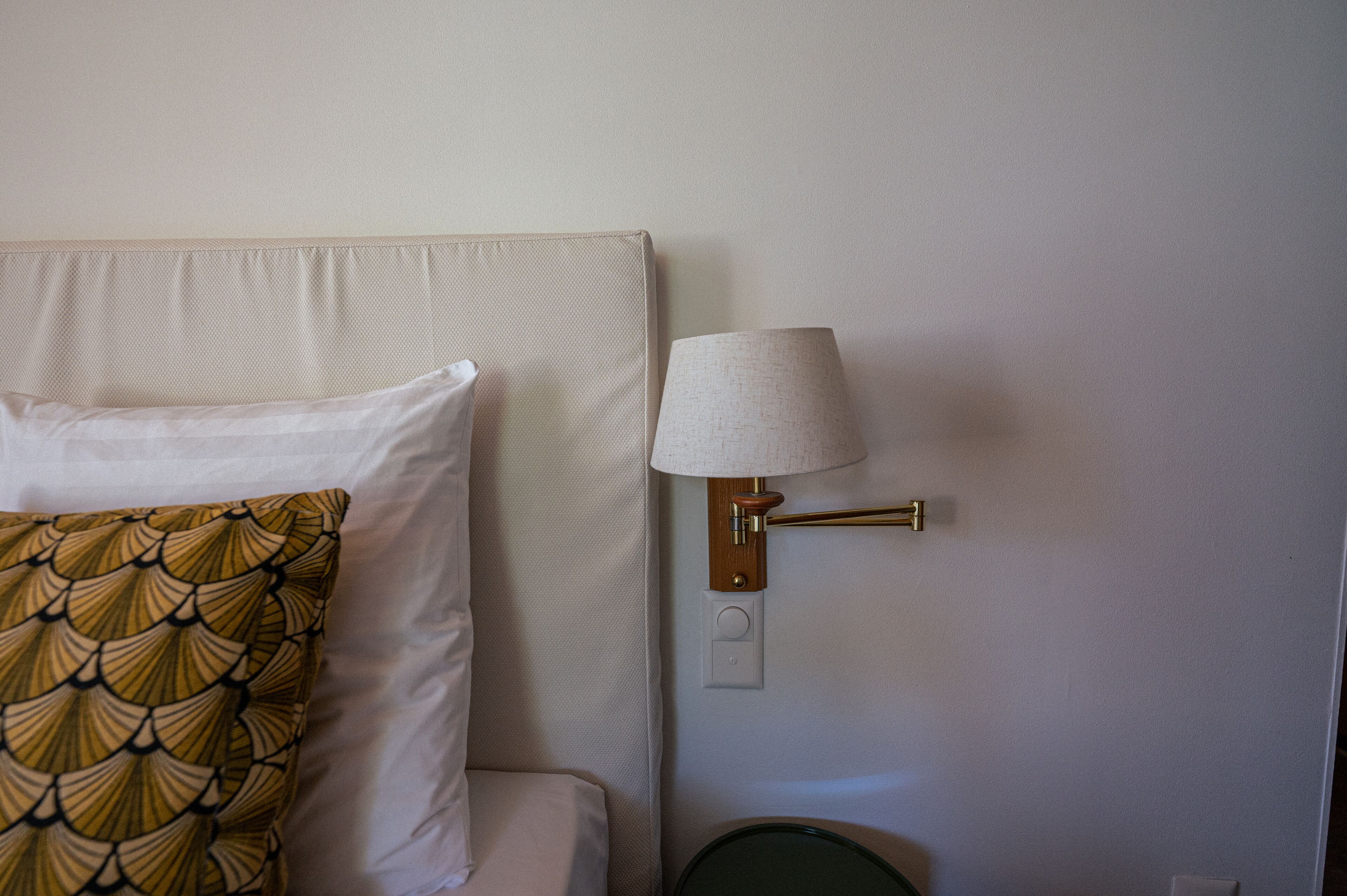 A hotel room with a bed, a nightstand, a lamp, and a wall socket.