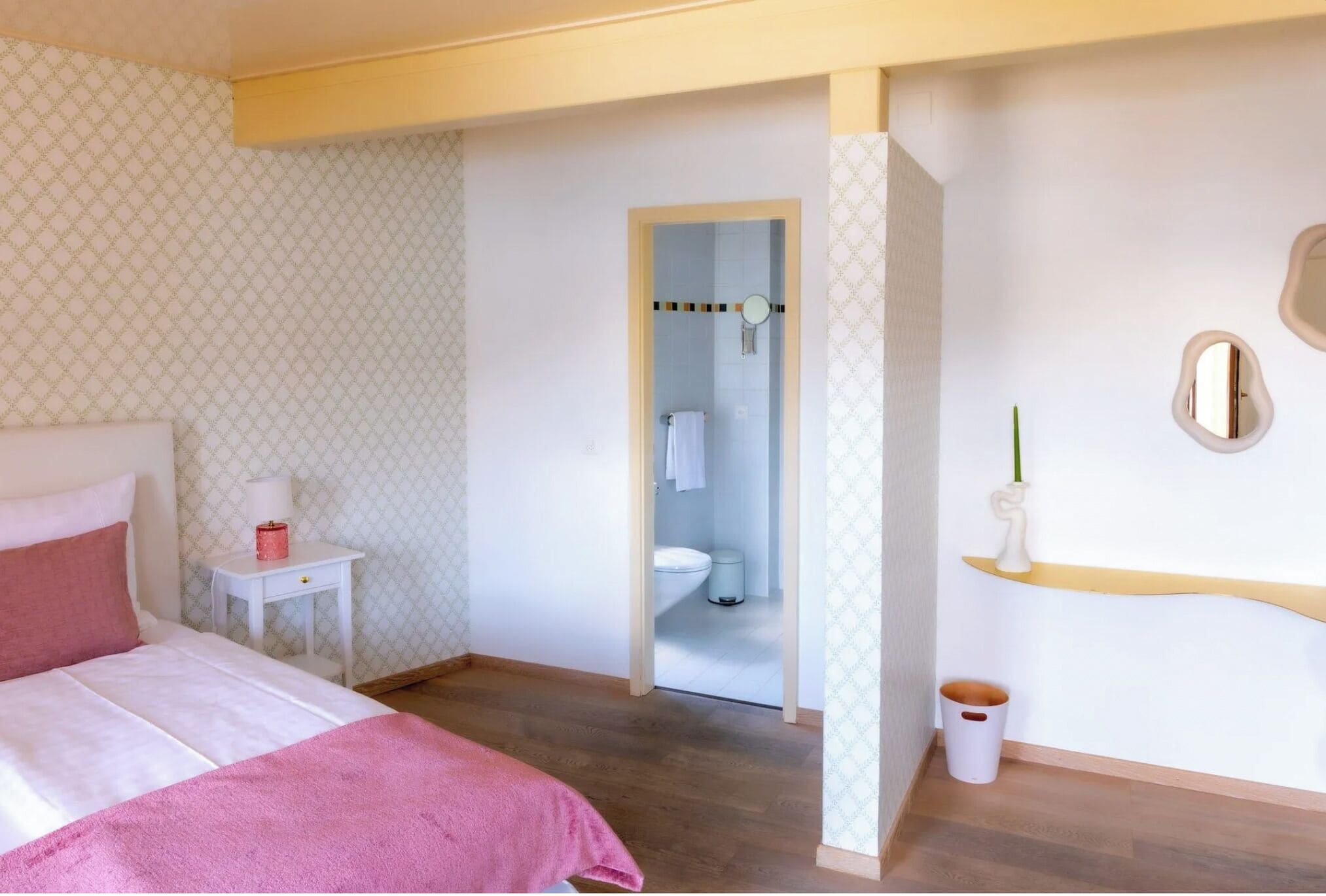 Un dormitorio con cama, mesita de noche y un baño visible a través de una puerta abierta.