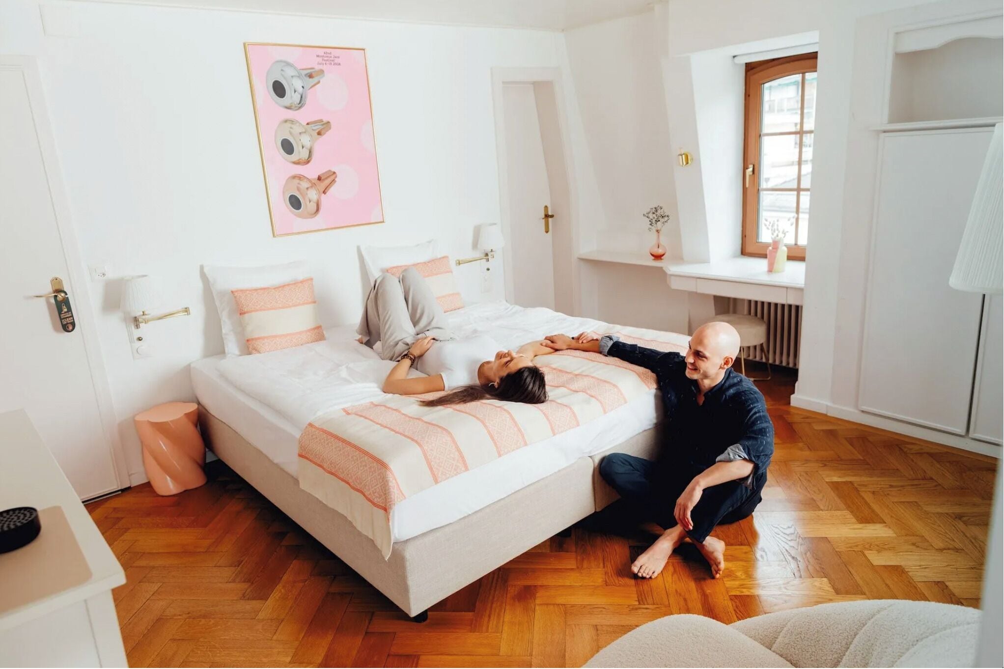 Un dormitorio con cama, mesitas de noche, una ventana y un cuadro en la pared.
