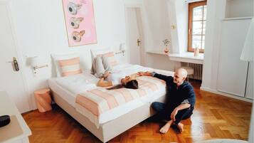 Un dormitorio con cama, mesitas de noche, una ventana y un cuadro en la pared.