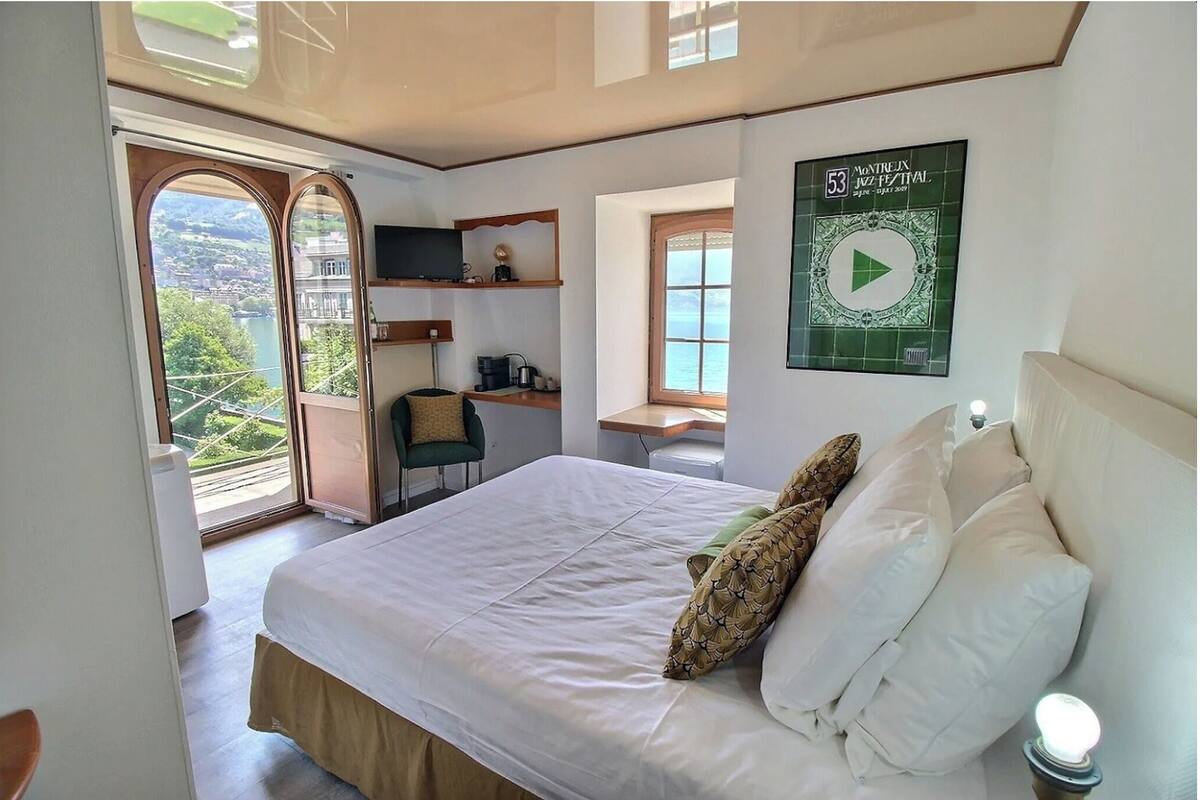 Ein Schlafzimmer mit Bett, Kissen, Schreibtisch, Stuhl, Fernseher und einem Fenster mit Meerblick.