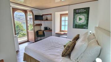 Ein Schlafzimmer mit Bett, Kissen, Schreibtisch, Stuhl, Fernseher und einem Fenster mit Meerblick.