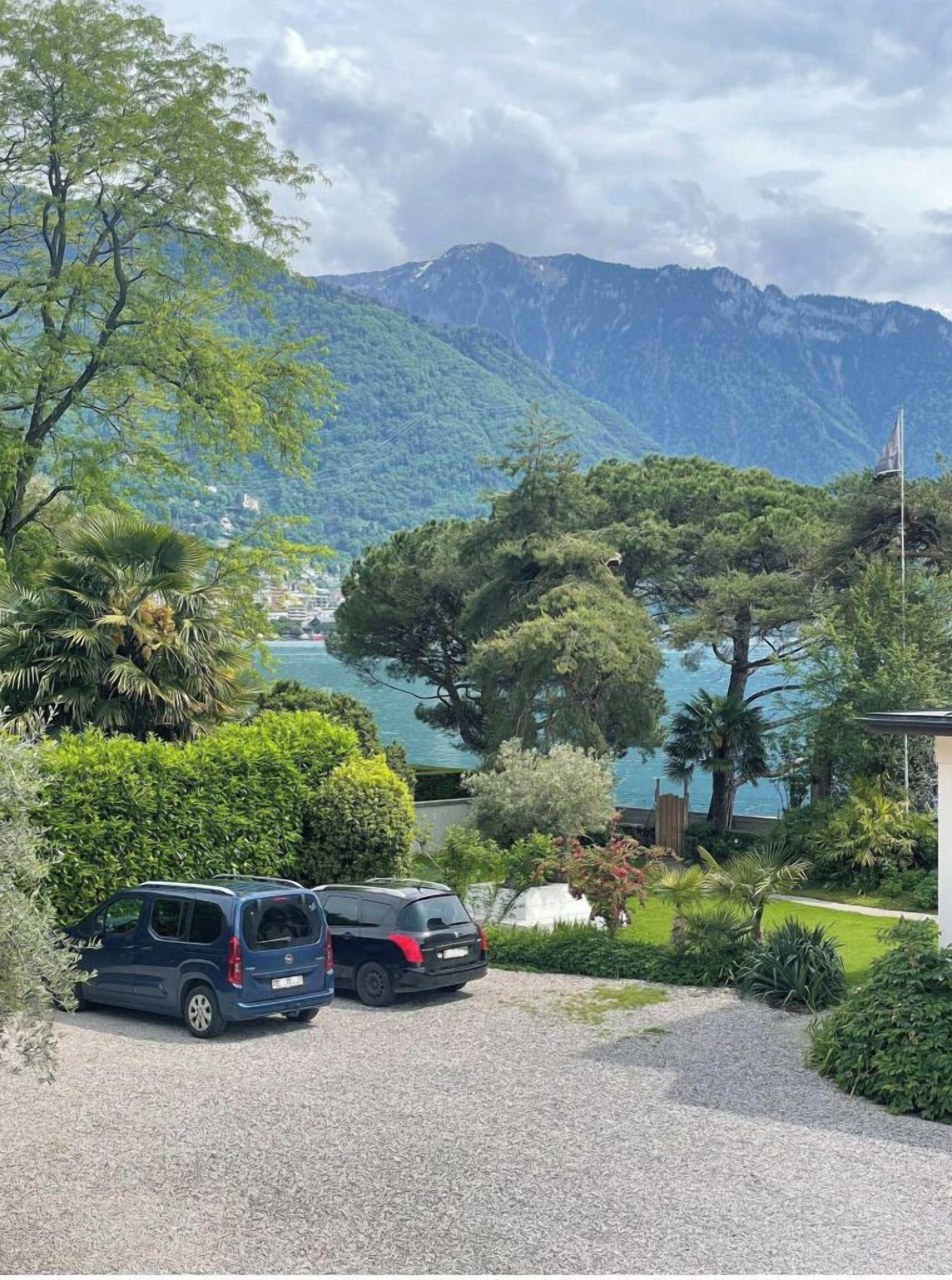 Una vista panorámica de una zona montañosa con un lago, dos coches aparcados y abundante vegetación.