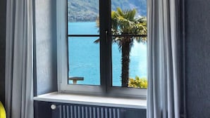Une chambre avec un lit, une fenêtre avec des rideaux et une vue sur un lac et des montagnes.