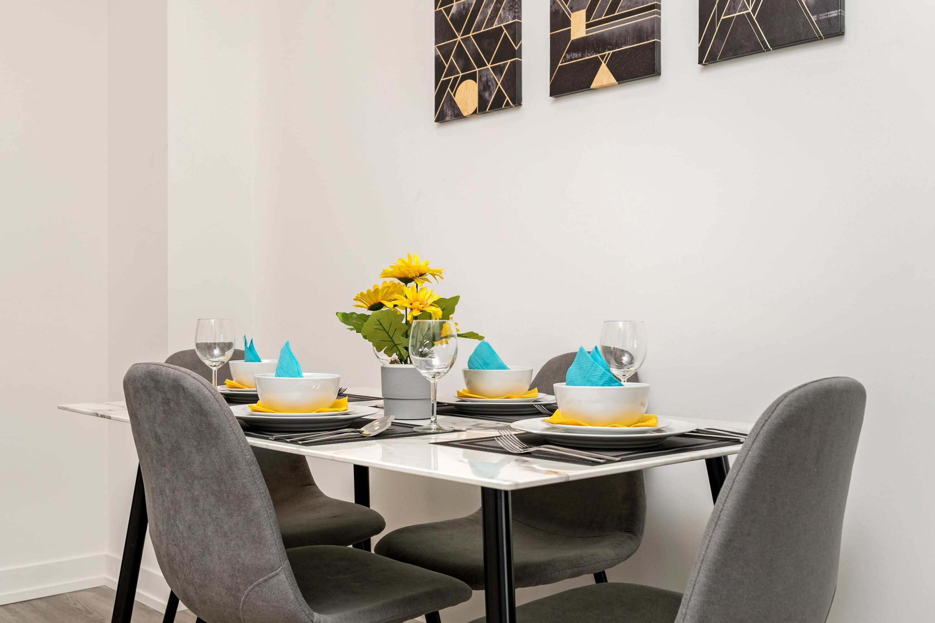 Et spisebord med stole, en vase med gule blomster og geometrisk vægkunst.
