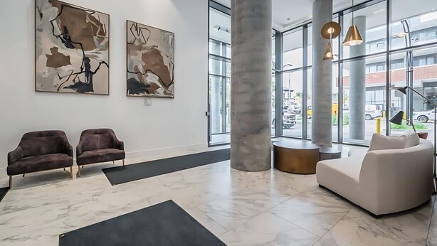 Un hall d’entrée moderne avec deux canapés, des œuvres d’art abstraites accrochées au mur, de grandes fenêtres et un pilier central.