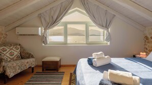 A bedroom with a large window, a bed, a chair, a bench, and an air conditioning unit. - Meganisi Villa Armonia - Private Pool Oasis (Vathi)