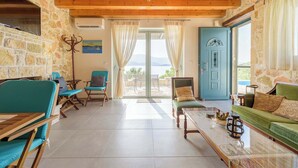 A spacious living area with stone walls, wooden ceiling beams, and a large sliding glass door leading to an outdoor patio. - Meganisi Villa Armonia - Private Pool Oasis (Vathi)