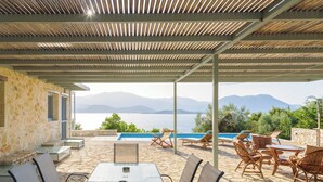 An outdoor patio with a table and chairs, a pool, and a view of the sea and mountains. - Meganisi Villa Armonia - Private Pool Oasis (Vathi)
