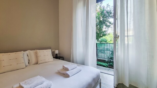 A bedroom with a bed, pillows, a nightstand, and a view of a balcony with a railing and greenery. - Italianway - Ozieri 7 (Milan)