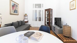 A modern living room with a grey sofa, a dining table with two mugs, a book, and a television on a stand. - Italianway - Ozieri 7 (Milan)
