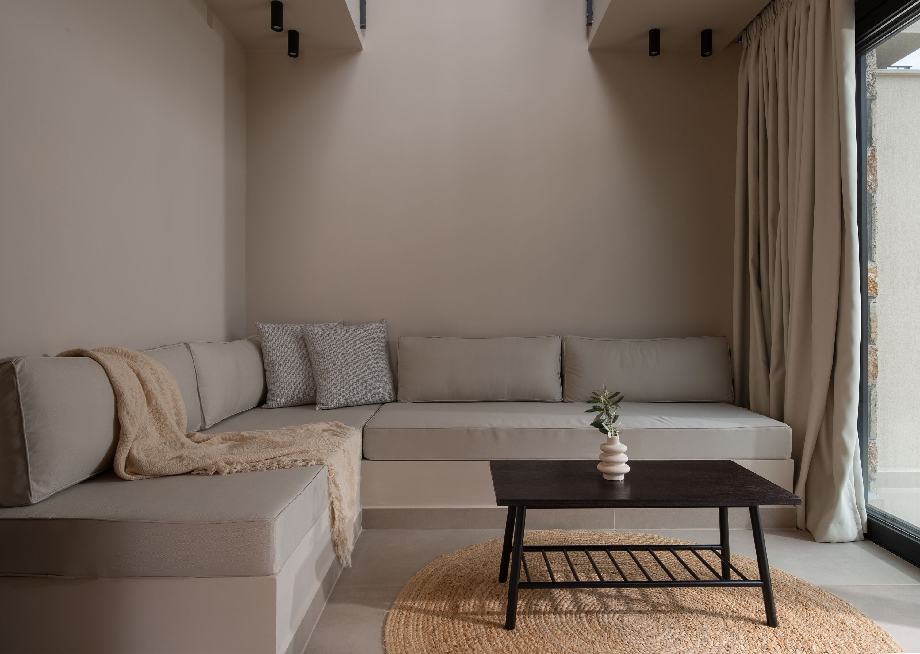 A modern living room with a beige sectional sofa, a small coffee table, and a large window with curtains.