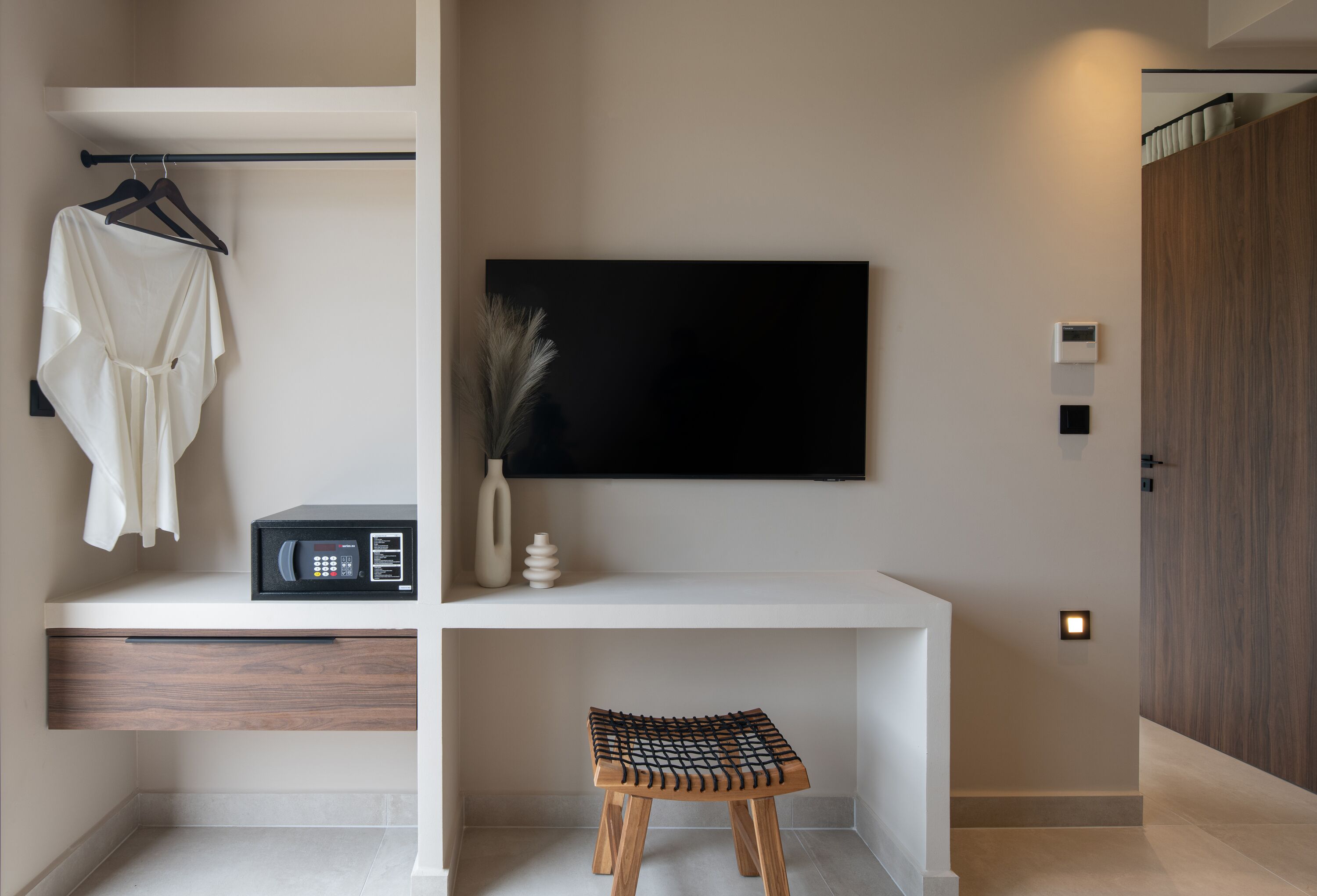 Een moderne badkamer met een witte wastafel, een ophangdouche, een zwarte magnetron, een vaas met gedroogde planten en een houten kruk.