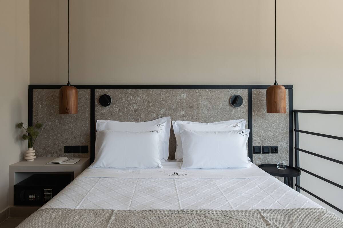 A neatly made bed with white linens, a headboard with a stone-like texture, and two pendant lights.