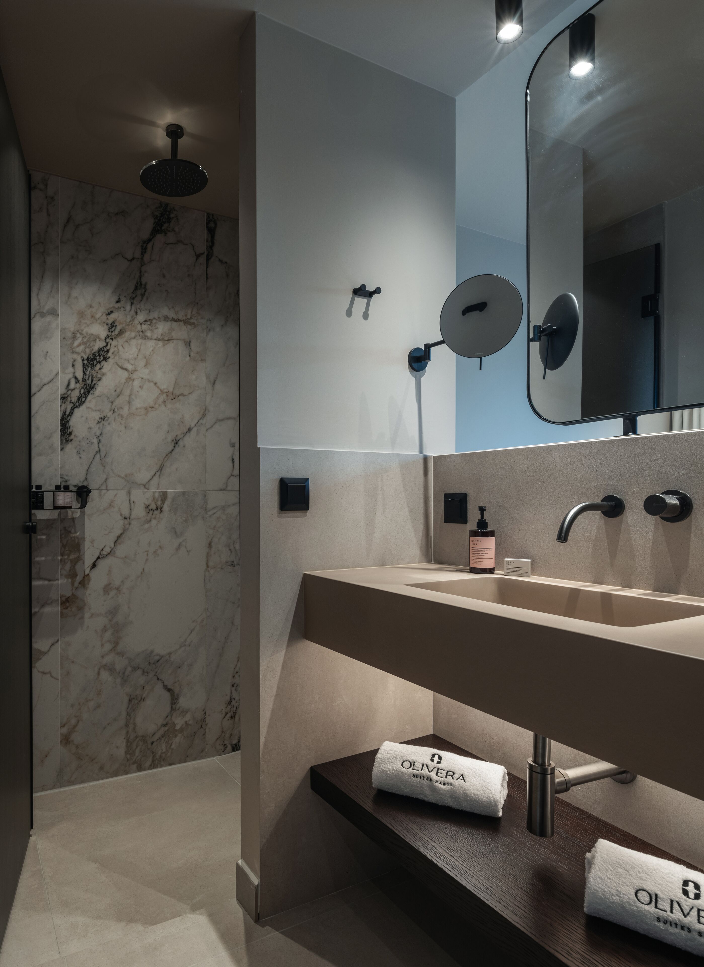 Un baño moderno con pared de mármol, un espejo grande, un lavabo y una ducha.