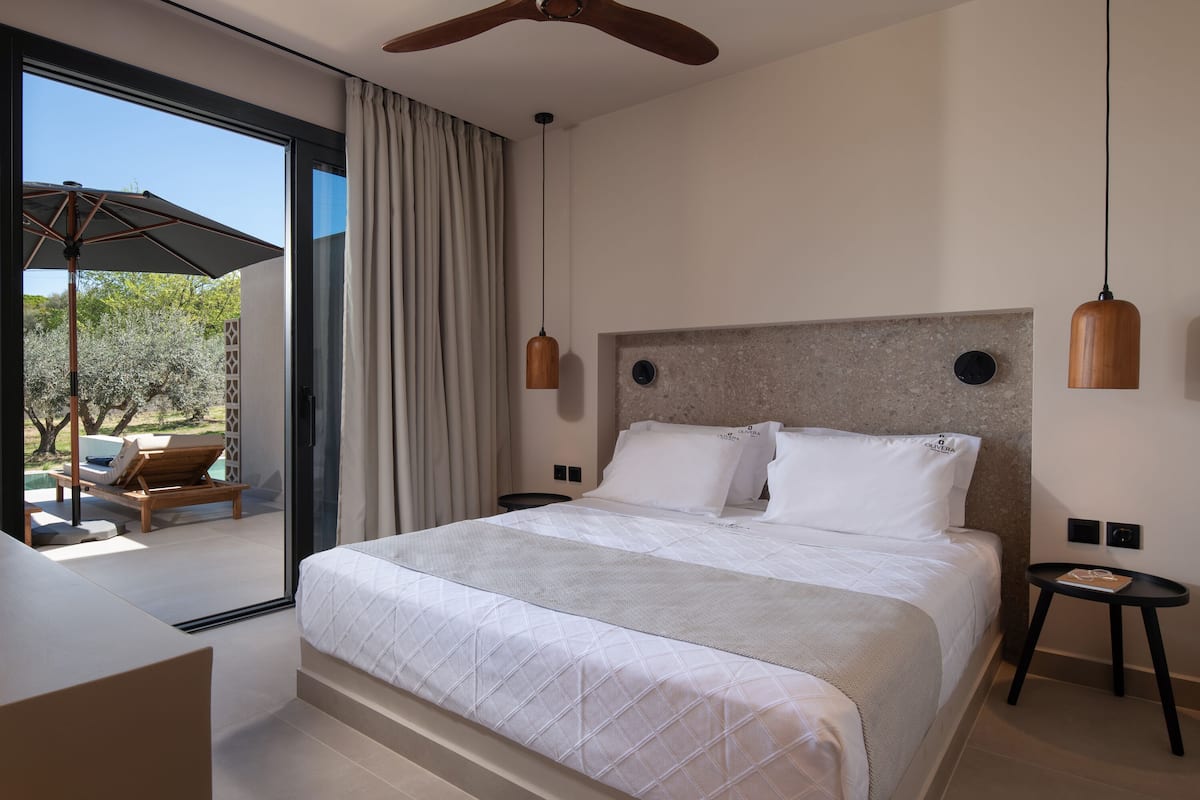 A modern bedroom with a large bed, a ceiling fan, and a view of an outdoor area with a patio and lounge chairs.