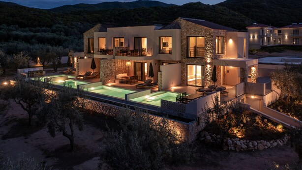 A modern multi-story house with a swimming pool, outdoor seating, and a view of the surrounding hills.