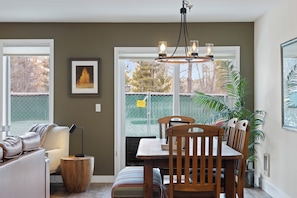 Un comedor con una mesa y sillas de madera, una lámpara colgante y vistas a través de una ventana.