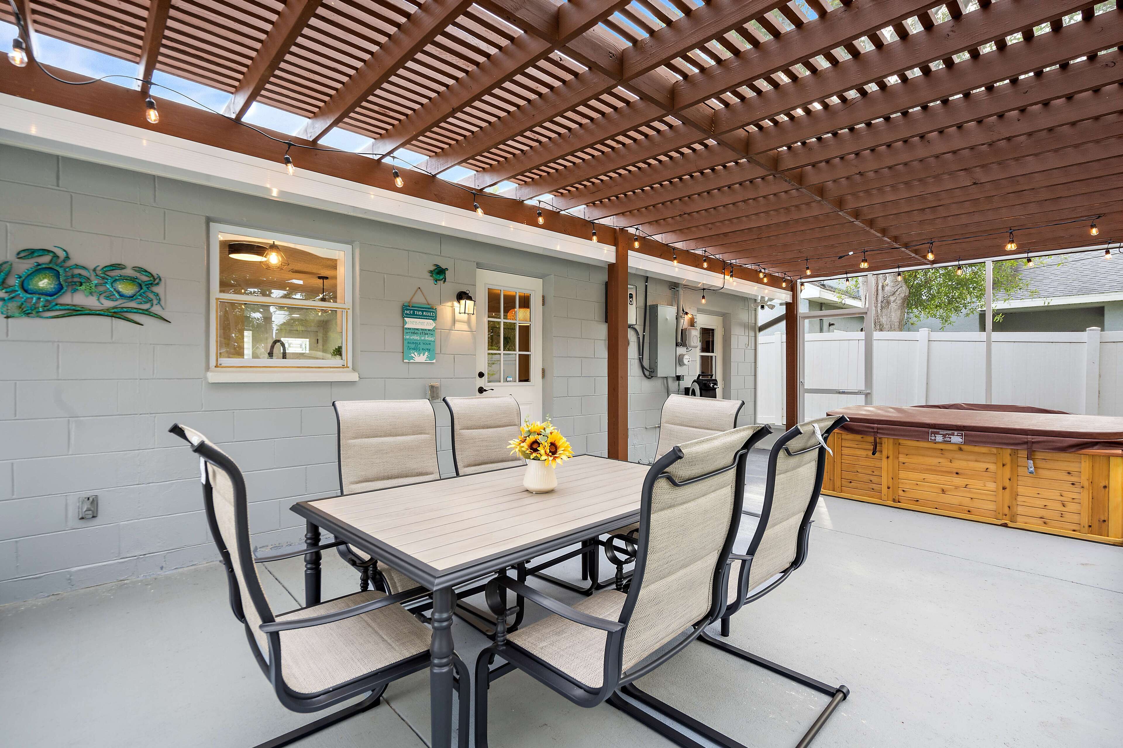 Um alpendre coberto com mesa e cadeiras, um banco de madeira e um objeto decorativo na parede.