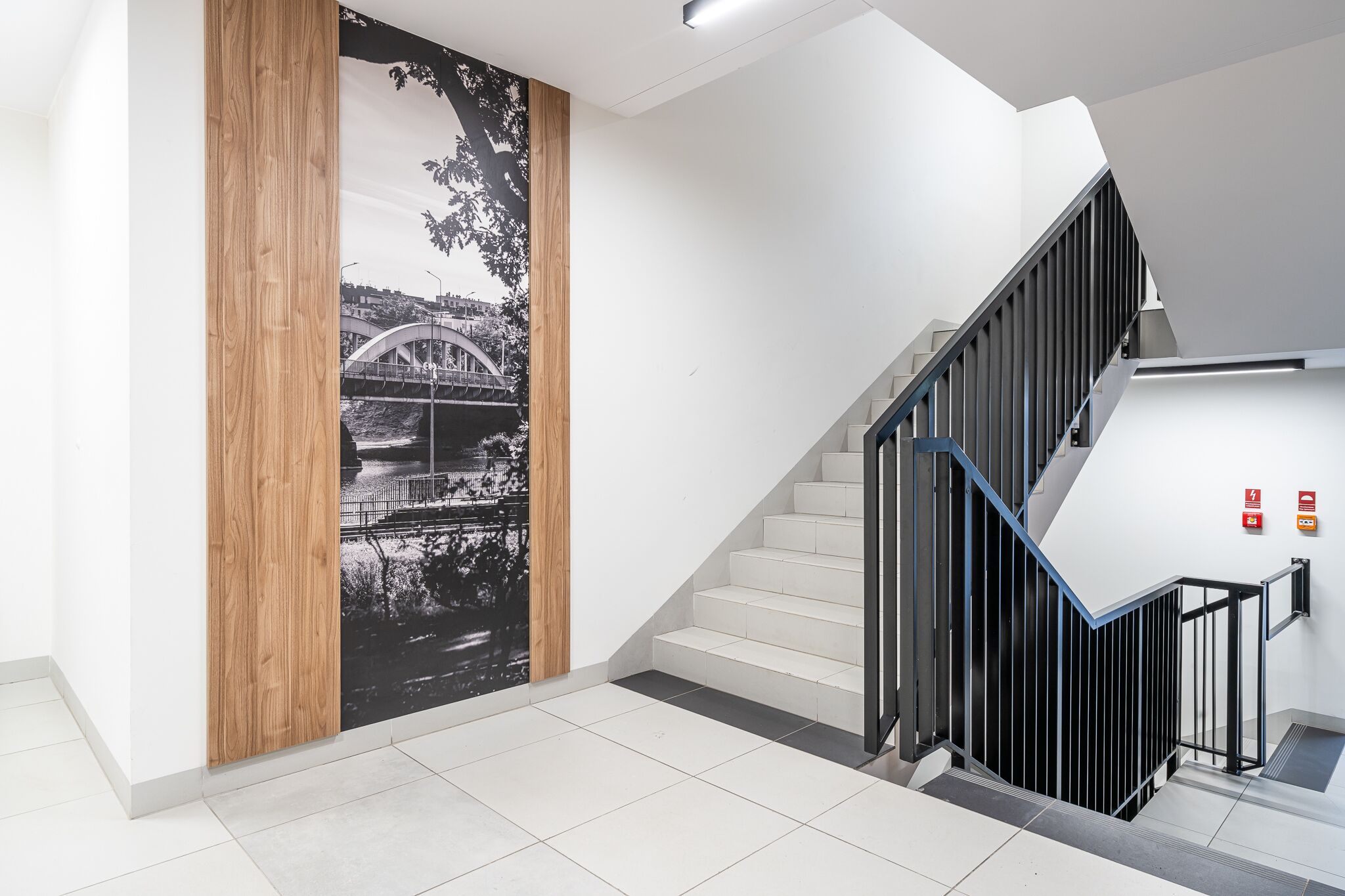 A modern interior with a staircase, a wooden panel with a black and white photograph, and a white wall.
