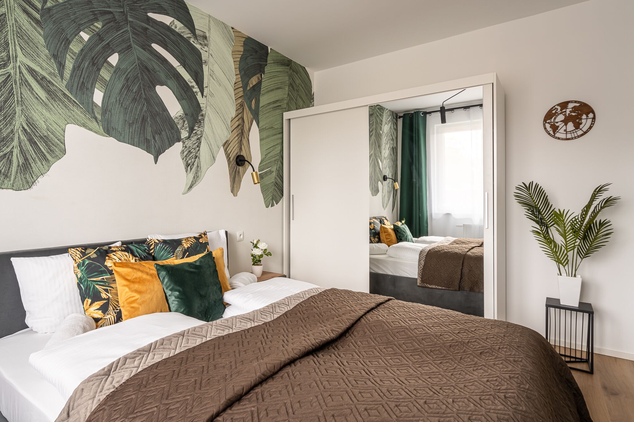 A modern bedroom with a large bed, a mirror, a potted plant, and a world map on the wall.