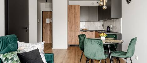 A modern kitchen with dark cabinets, a wooden door, and a dining area with green velvet chairs and a round table.